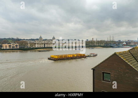 Lastkahn ziehen gelbe Container an der Themse und Greenwich auf der Durchreise. Nachmittag an einem Wintertag mit bewölktem Himmel geschossen.  Abfallentsorgung Stockfoto