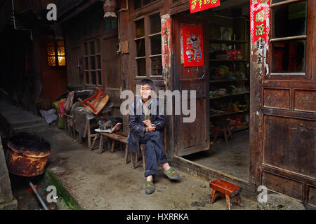 Zengchong Dorf, Guizhou, China - 12. April 2010: chinesische Mann sitzt neben einem ländlichen Marktstand in einem Holzhaus, er beschlagen im grünen Turnschuhe und Stockfoto