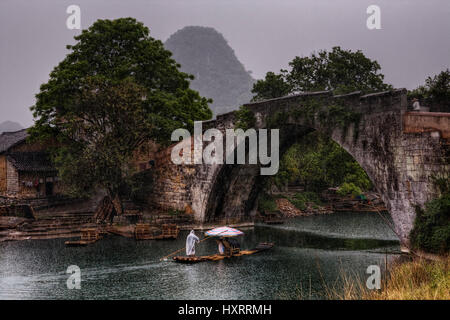 Yangshuo, Guangxi, China - 31. März 2010: Dragon Bridge im Yulong Dorf, machen Touristen eine Flussfahrt auf einem Bambus-Boot, bei strömendem Regen. Stockfoto