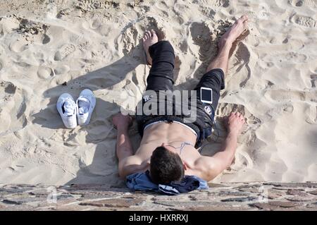 Junger Mann, Faulenzen am Strand anhören von MP3-player Stockfoto