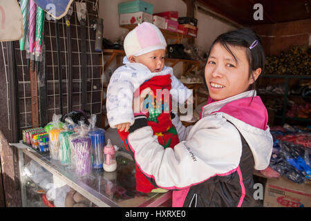 Zhaoxing Dong Dorf, Guizhou Provinz, China - 8. April 2010: Junge asiatische Ladenbesitzer Frau stehen an der Theke mit einem Baby im Arm, ein Graf Stockfoto