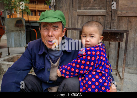 Zhaoxing Dong Dorf, Guizhou Provinz, China - 9. April 2010: Dreijähriges Kind umarmt einen älteren Mann, der in seinem Mund Pfeifenrauchen hält. Stockfoto