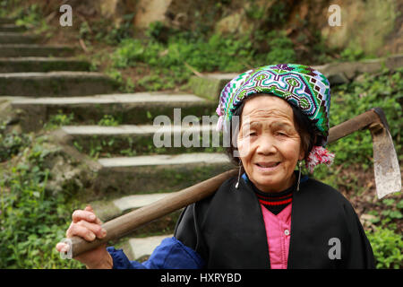 PINGAN Dorf, Provinz Guangxi, China - 5. April 2010: Älterer Bauer Bäuerin kommt den Berg hinunter die Schritte der steinerne Treppe mit einer Hacke Stockfoto