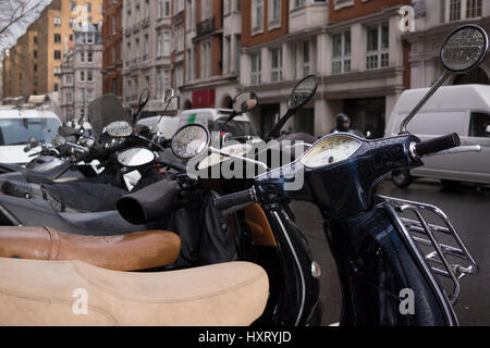 Eine Reihe von Vespa Roller parkten auf einer Straße in London, Mayfair nach dem Regen. Viele Menschen haben sich an Motorrädern für die City-Maut vermeiden gewandt. Stockfoto