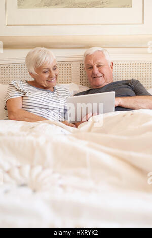 Gerne älteres Paar mit einem digitalen Tablet zusammen im Bett Stockfoto