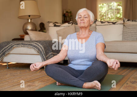 Ältere Frau sitzt im Lotussitz meditieren zu Hause Stockfoto
