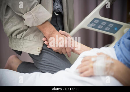 Ein alte Frauen kranke Patienten auf Bett mit ihrem Mann die hand im Krankenhaus zur medizinischen Hintergrund Stockfoto