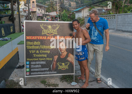 Kru Sak, eine Muay Thai oder Thai-Boxer, stellt neben einer Plakatwand Funktionen seinem Fitness-Studio während ein westlicher Tourist in Phuket, Thailand sich schließt. 9. März 2017 Stockfoto