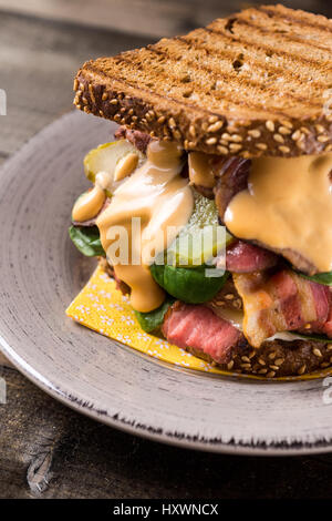Große hausgemachte Sandwich mit Roastbeef, Speck, Gurken, Baby-Spinat und Krautsalat Dressing in geröstetem Brot Stockfoto