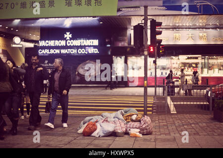 Eine Obdachlose chinesische Dame schläft zwischen ihre Koffer auf einer Straße in Hong Kong, China. Stockfoto