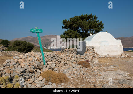 grüne Wegweiser in eine Steinmauer mit weißen kleinen Kapelle und Kiefer Baum über Livadia auf dem Weg zum alten Dorf Gera, Tilos, Dodekanes, Griechenland Stockfoto