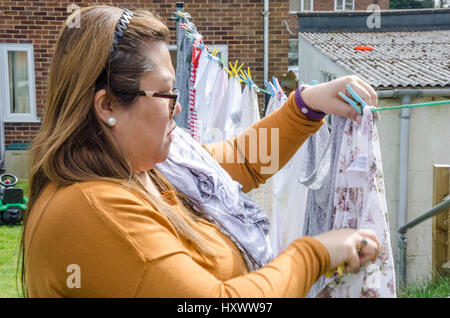 Eine Dame, hängende Kleidung auf einer Wäscheleine im Garten hinter dem Haus. Stockfoto