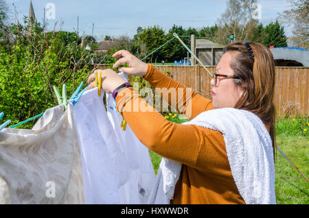 Eine Dame, hängende Kleidung auf einer Wäscheleine im Garten hinter dem Haus. Stockfoto