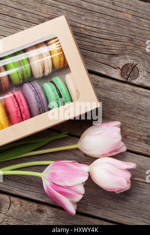 Bunte Makronen Plätzchen und rosa Tulpen Strauß auf Holztisch. Ansicht von oben Stockfoto