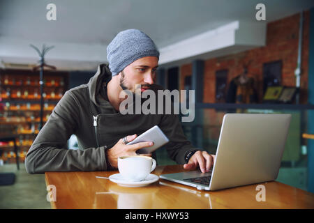 Junge hübsche Hipster Mann mit Bart ist in Cafeteria Computer verwenden. Stockfoto