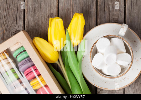 Bunte Makronen Plätzchen und gelbe Tulpen Strauß auf Holztisch. Ansicht von oben Stockfoto