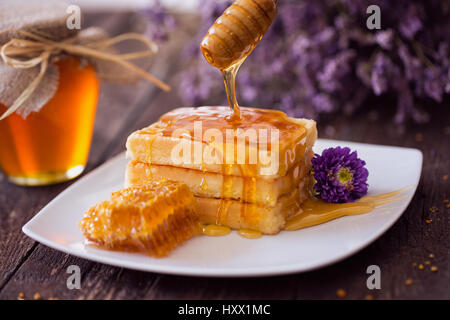 Tropfen Honig aus einem hölzernen Wagen auf frisch gebackene Waffel Stockfoto