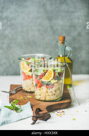 Gesunde vegane Energie fördernde Salat mit Quionoa, Avocado, getrockneten Tomaten, Basilikum, Olivenöl, Minze im Glas, Marmor Hintergrund, Tiefenschärfe, c Stockfoto