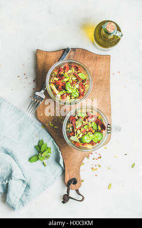 Gesunde vegane Energie fördernde Salat mit Quionoa, Avocado, getrockneten Tomaten, Basilikum, Olivenöl, Minze im Glas, Marmor Hintergrund, Ansicht von oben. Sauber ea Stockfoto