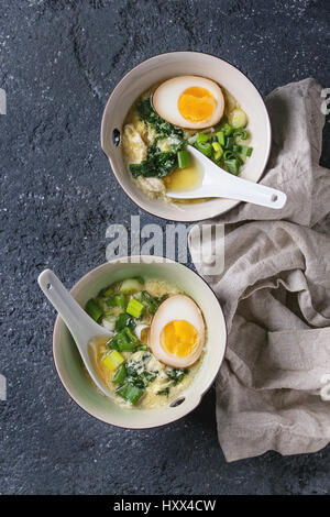 Zwei Schalen mit asiatischen Stil Suppe mit Rührei, die Hälfte der marinierte Ei, Frühlingszwiebeln, Spinat serviert mit weißen Löffel und Textil über schwarzer text Stockfoto