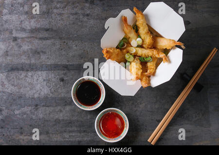 Fried-Tempura-Garnelen mit Reis und Frühlingszwiebeln in Pappschachtel zum mitnehmen. Serviert mit Saucen, Stäbchen über alte Metall Hintergrund. Ansicht von oben, Raum. Asiatische Stockfoto