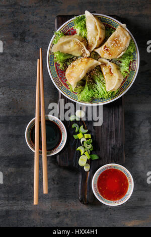 Gyozas Potstickers auf Eisbergsalat mit Saucen. Serviert im traditionellen Porzellanplatte mit Stäbchen und Frühlingszwiebeln auf Holz dienen Board über alte erfüllt Stockfoto