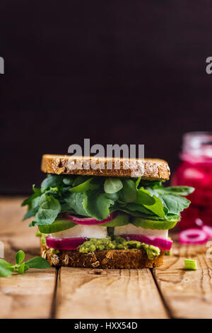 Eine Frühling-Feta-Sandwich mit Avocado, eingelegten roten Zwiebeln und Kräuter wie Portulak, Rucola und frischer Minze serviert auf einem Holzbrett aus fotografiert Stockfoto