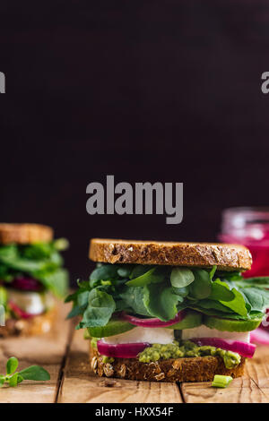 Frühling-Feta-Sandwiches mit Avocado, eingelegten roten Zwiebeln und Kräuter wie Portulak, Rucola und frischer Minze serviert auf einem Holzbrett aus fotografiert Stockfoto