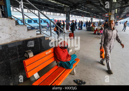 Am frühen Morgen in New Delhi Railway station Plattform, New Delhi, Punjab Zustand, Hauptstadt von Indien, Passagier Einschlafen im Schneidersitz auf orange Holzbank Stockfoto