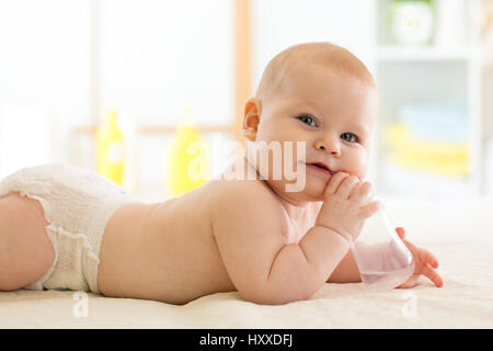 Hübsches Babymädchen trinkt Wasser aus der Flasche auf Bett liegend. Kind weared Windel im Kinderzimmer. Stockfoto