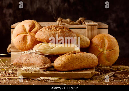 Nahaufnahme einer Auswahl an verschiedenen Brötchen und einige Ähren auf einem rustikalen Holztisch Stockfoto