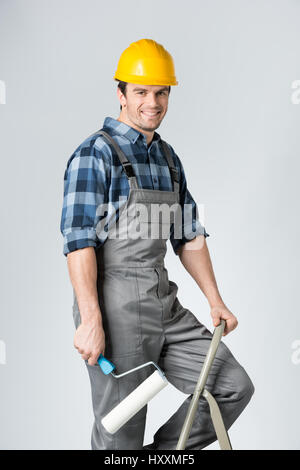 Lächelnde Arbeiter mit Paint Roller stehen auf Leiter Stockfoto
