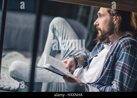 Junge bärtige Mann hält Buch und nachdenklich wegschauen Stockfoto