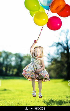 Blonde Mädchen springen mit Haufen bunte Luftballons auf dem Lande Stockfoto