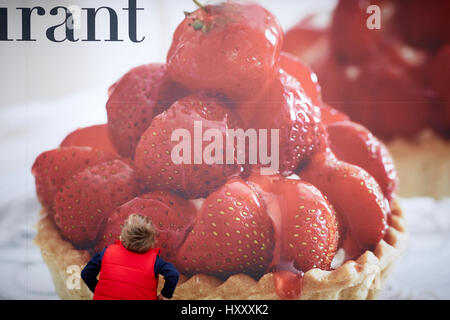 Kleines Kind suchen bei großen Strawberry Tart-Werbeplakat. Stockfoto