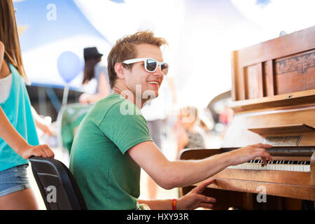 Teenager-Paar beim Sommer-Musikfestival, hübscher kleiner Junge spielt Klavier. Sonniger Tag. Stockfoto