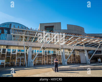 Ein einziger Polizist, der an einem warmen, sonnigen Tag die Front des schottischen Parlamentsgebäudes bewacht, Holyrood, Edinburgh, Schottland. Stockfoto