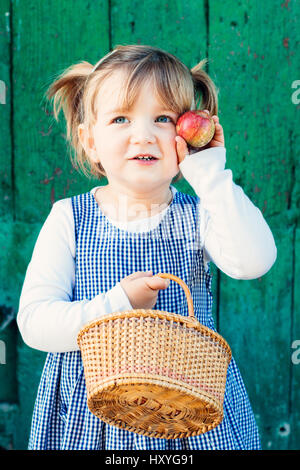 Stolz und niedliche kleine Mädchen mit einem karierten Kleid und einem Korb zeigen die Apple hat sie abgeholt Stockfoto