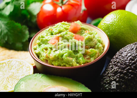 Guacamole Schüssel mit Zutaten und Tortilla-Chips auf einem blau lackierten Holztisch. Stockfoto