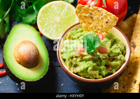 Guacamole Schüssel mit Zutaten und Tortilla-Chips auf einem blau lackierten Holztisch. Ansicht von oben Stockfoto