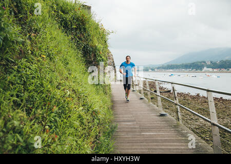 Attraktive Mann läuft auf einem Holzsteg über dem Meer. Tägliches Training. Stockfoto