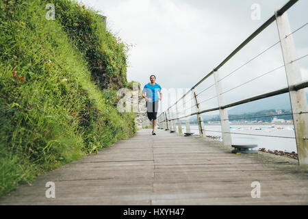 Attraktiver Mann läuft auf einem Holzsteg direkt am Meer. Tägliches Training. Stockfoto