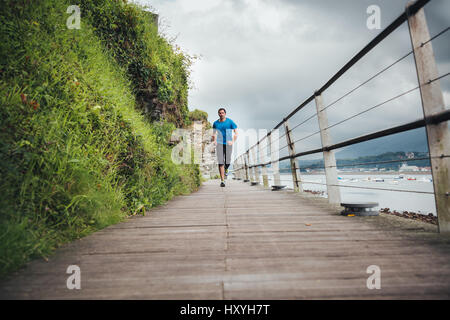 Attraktiver Mann läuft auf einem Holzsteg direkt am Meer an einem stürmischen Tag. Einsame tägliches Training. Stockfoto