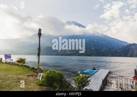 Bootsanlegestelle im Vordergrund und Cloud-bedeckten vulkanischen Berge in der Ferne am Lake Atitlan, Guatemala, Mittelamerika. Stockfoto