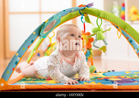 Glückliche sieben Monate baby Mädchen spielt auf bunte Krabbeldecke liegend Stockfoto