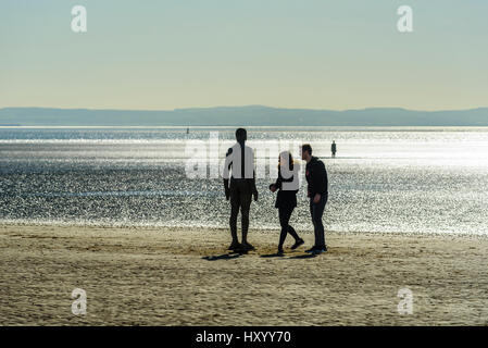 Besucher betrachten Sie eine der 100 gusseisernen Figuren bilden Another Place von Anthony Gormley, Crosby Strand, Merseyside Stockfoto