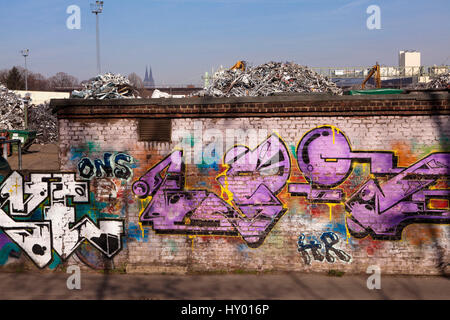 Deutschland, Köln, Schrott Hof mit alten Metall im Stadtteil Deutz, im Hintergrund die Kathedrale, Wand mit Graffiti. Stockfoto