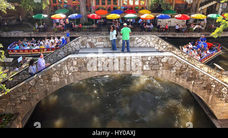 Touristen, die über eine Brücke an der San Antonio River Walk als Tourenboot geht unter in San Antonio, Texas Stockfoto