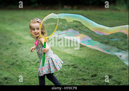 Young Bond Girl bläst eine riesige Seifenblase im Park Stockfoto