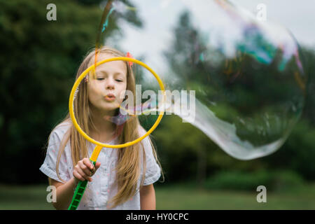 Young Bond Girl bläst eine riesige Seifenblase im Park Stockfoto